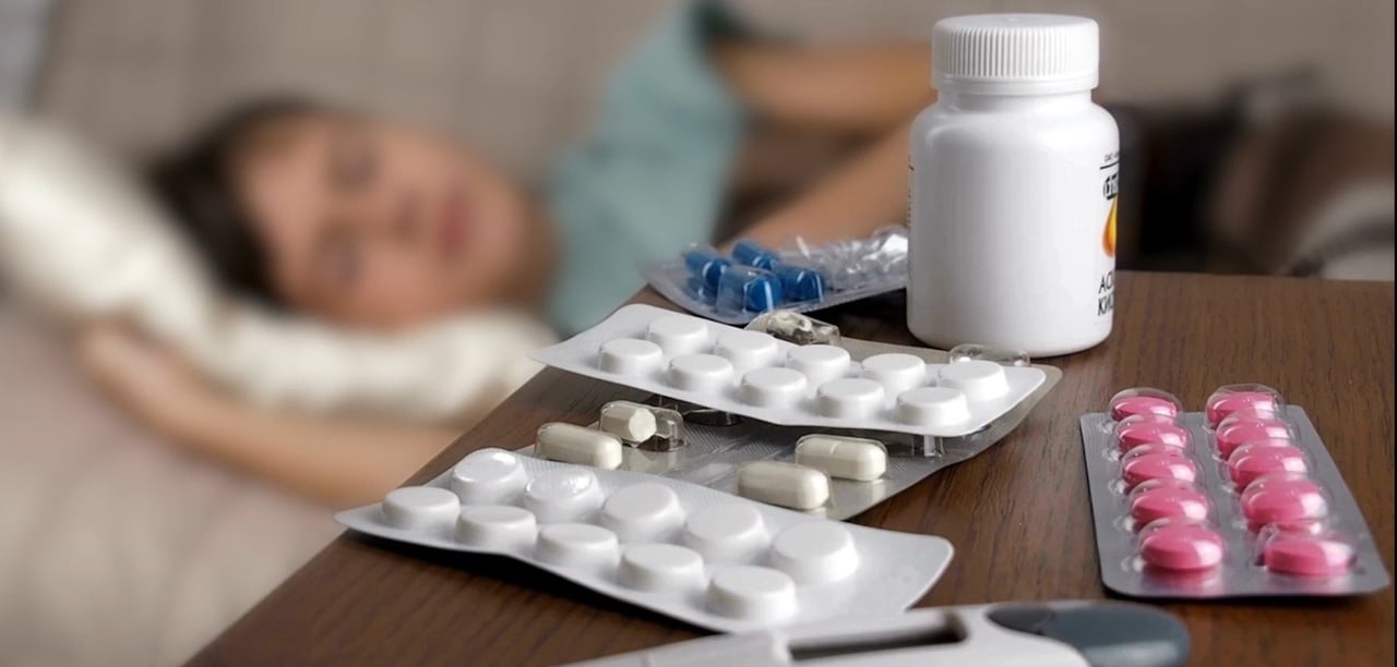 Image depicting sick perosn in bed with pills on side table