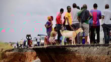 Locals stand beside a damaged section of the road with a goat after Cyclone Idai